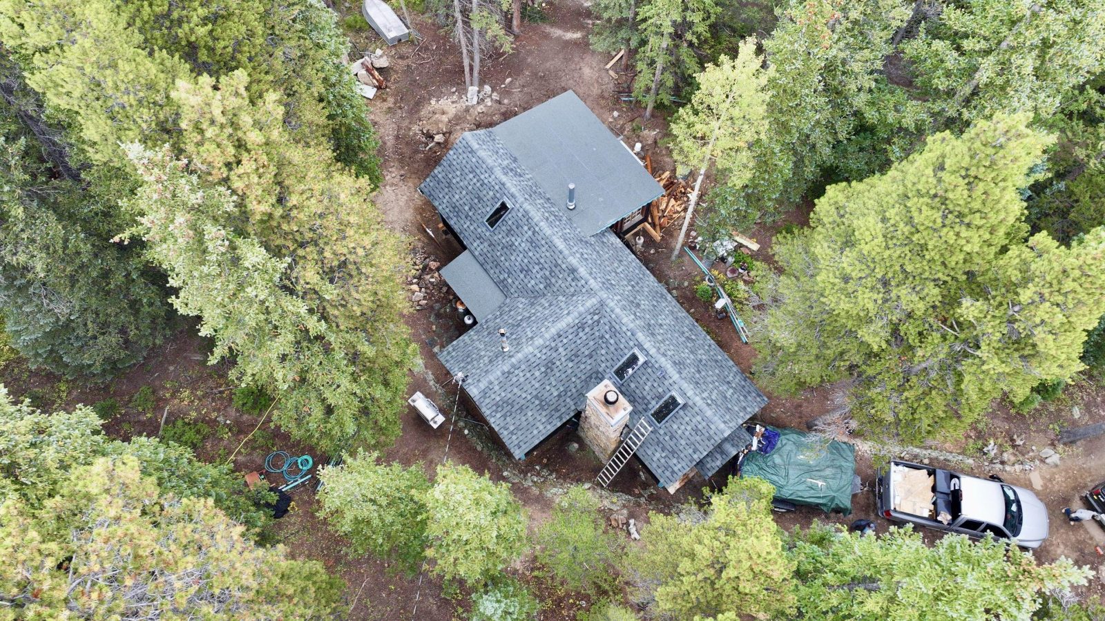 Mountain Cabin with Limited Defensible Space Aerial view of a mountain cabin surrounded by dense evergreen trees in Colorado, showing limited defensible space and wildfire risk around the structure.